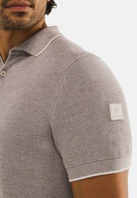 Polo shirt met korte mouwen in lichtgrijs textuurgebreid. Bevat een witte kraag met contrasterende rand, twee knopen en een logo patch op de linker mouw.