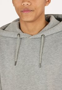 Grijze hoodie met een gestructureerde stof. Voorzien van een trekkoord met metalen tips en een grote capuchon. Close-up van het nekgebied.
