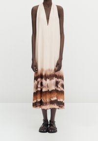 Robe dos nu crème avec un motif tie-dye, passant du brun clair au brun foncé à l'ourlet ; associée à des sandales noires à brides.