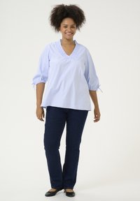 Blusa de rayas azul clara con escote en V con volantes y mangas abullonadas, combinada con jeans de mezclilla azul oscuro y zapatos planos negros.