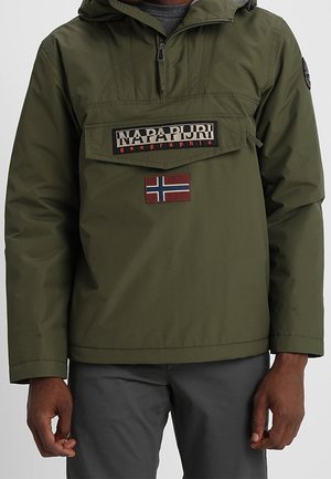 Homme portant une veste Napapijri vert olive avec poche avant et écusson du drapeau norvégien, portée avec un pantalon gris foncé.