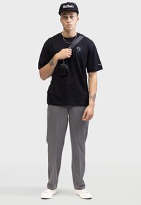 Black cotton t-shirt with blue graphic, gray tailored pants, white sneakers, and a black cap. Small black bag hangs from shoulder strap.