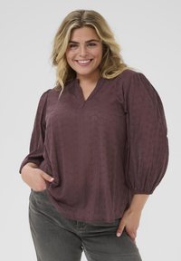 Plum-colored blouse with a v-neck, balloon sleeves, and textured pattern. Made of lightweight fabric with subtle floral embroidery accents.