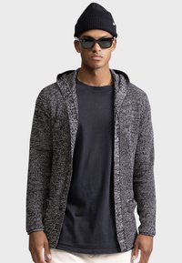 Black and gray knit hooded cardigan with open front, textured fabric, long sleeves, and side pockets, layered over a black shirt.
