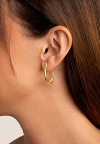 Orecchino a cerchio d'oro attaccato all'orecchio, caratterizzato da un design elegante e curvato con una finitura lucida e una texture liscia.