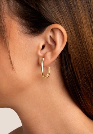Goldener Ohrstecker, der am Ohr befestigt ist, mit einem eleganten, geschwungenen Design, glänzender Oberfläche und glatter Textur.