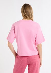 Roze katoenen T-shirt met een relaxte pasvorm, korte mouwen en een ronde halslijn. Draagt daarbij geruite rode en witte broek met patroon.