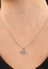 Srebrny naszyjnik z zawieszką w kształcie serca, z symbolem nieskończoności splecionym razem, ozdobiony małymi przezroczystymi kamieniami szlachetnymi, które dodają blasku.