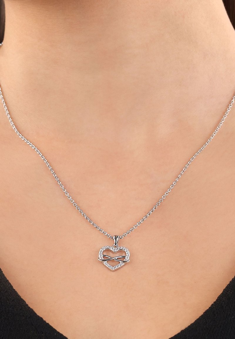 Srebrny naszyjnik z zawieszką w kształcie serca, z symbolem nieskończoności splecionym razem, ozdobiony małymi przezroczystymi kamieniami szlachetnymi, które dodają blasku.