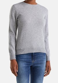 Světle šedý svetr z měkkého, strukturovaného materiálu s kulatým výstřihem a žebrovanými manžetami, kombinovaný s modrými džíny pro ležérní vzhled.