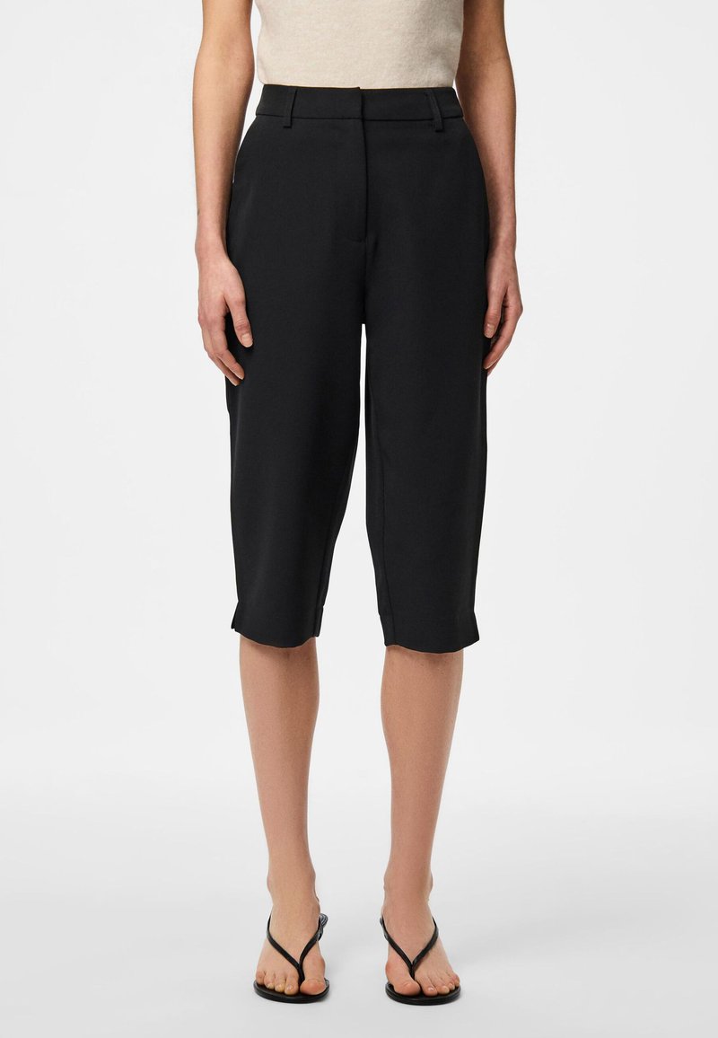 Black tailored capri pants with a smooth texture, featuring a mid-rise waistband and rolled hems, paired with black flip-flops.