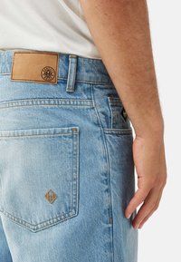 Ljusblå denimjeans med en beige läderlapp, utrustade med orange sömmar och en bakficka med en diamantlogotyp.