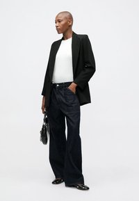 Blazer nero su misura, top bianco aderente, jeans larghi scuri e borsa nera. Tessuto morbido, design strutturato, look casual ma curato.