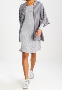 Abito grigio a maglia con scollatura quadrata, abbinato a un kimono a righe grigie e bianche. La modella indossa sneaker argentate e ha i capelli ricci.