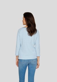 Langärmliges Shirt mit blauen und weißen Streifen, Design mit Rundhalsausschnitt, gerippte Textur, kombiniert mit hellblauen Jeans, von hinten zu sehen.