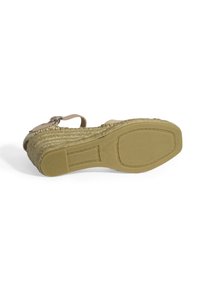 Sandale compensée avec une semelle en style espadrille tissée, des brides beiges et une fermeture à boucle. Semelle extérieure en caoutchouc avec des rainures texturées pour une meilleure adhérence.