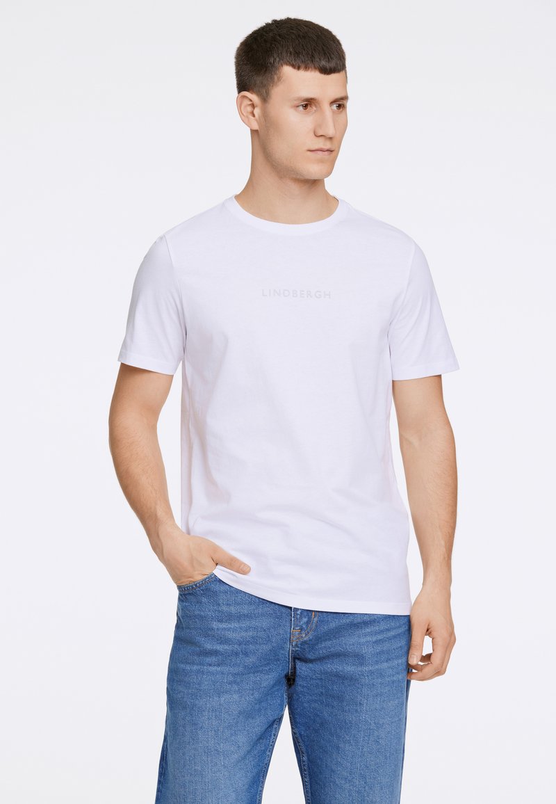 Valkoinen puuvillapaita, jossa on pyöreä kaula-aukko ja lyhyet hihat; etupuolella on hillitty "LINDBERGH" -teksti. Yhdistetty sinisiin farkkuihin.