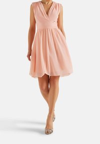 Meruňkově růžové šifonové šaty s výstřihem do V, plisovaným tělem a rozšířenou sukní. Doplněné o páskovou metalickou obuv a hladkou texturu.