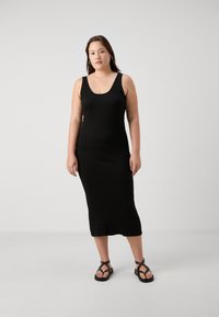 Svart ribbet maksikjole med rund hals og brede stropper, sammen med kraftige svarte sandaler. Enkel, tettsittende silhuett med ankel lengde.