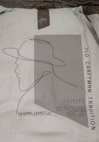 Beigen Stoffinterieur mit einer schwarzen Kontur eines Huts und Gesichts. Text enthält "ALTE HANDWERKSTRADITION" und Koordinaten. Markenlabel "Gipsy" angebracht.