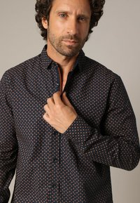 Marineblauwe overhemd met een herhalend geometrisch patroon in oranje. Voorzien van een klassiek kraag, lange mouwen en knoopsluiting.