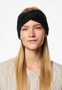 Fascia per capelli nera, attorcigliata, con una superficie texture indossata da una persona; presenta bordi lisci e si adatta saldamente attorno alla testa.