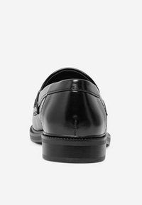 Zapato de vestir de cuero negro con un acabado liso, punta redondeada y tacón bajo apilado. La parte trasera presenta detalles de costura mínimos.