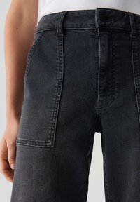 Pantaloni in denim nero con una superficie textured e design a cinque tasche. Presentano un'alta vita e dettagli di cucitura sottili sui lati.