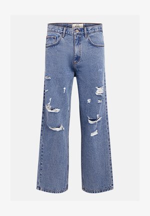 Kék, bőszárú farmernadrág, több szakadt és kopott részlettel az elülső combokon és térdeken, gombos és cipzáros záródással, valamint övszalagokkal.