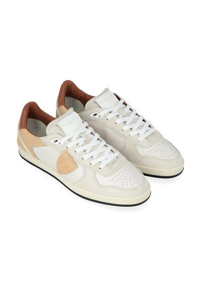 Baskets en cuir blanc avec accents beige, embout perforé, lacets blancs, col rembourré et semelle noire. Matériaux lisses et texturés utilisés.