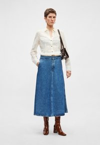 Balta, ar tekstūru, blūze ar pogu aizdari, kopā ar zilu džinsa maxisvārku un brūnām ādas augstpapēžu zābakiem. Tumši brūna plecu soma.