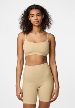 Beige seamless bralette and high-waisted shorts set. Soft, stretchy fabric; minimal design with thin straps and no visible seams.