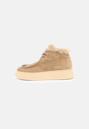 Bottine en daim marron clair avec doublure en fausse fourrure beige, bout rond, lacets à l'avant et semelle épaisse en caoutchouc beige sur fond blanc.