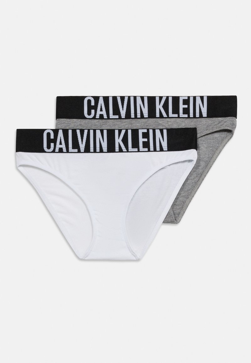 Δύο ζευγάρια εσωρούχων Calvin Klein, ένα λευκό και ένα γκρι, καθένα με μαύρη μέση που φέρει μεγάλο λευκό κείμενο "CALVIN KLEIN".