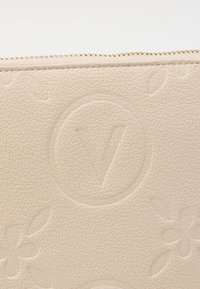 Primer plano de cuero beige texturizado con monograma Louis Vuitton en relieve y detalle de cremallera dorada.
