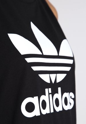 Czarny strój z dużym białym logo Adidas trefoil i nazwą marki w okolicy klatki piersiowej.