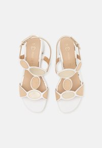 Hvite og beige sandaler med sirkulære detaljer, glatt lær, lav hæl og ankelremmer. Innesålen har en logo i gull.