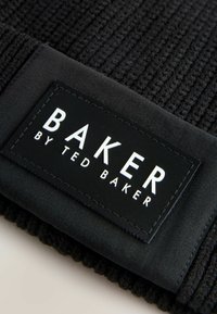 Schwarzer Stoff mit einem rechteckigen Etikett, auf dem "BAKER by TED BAKER" in weißen Buchstaben steht, was ein modernes Branding-Design zeigt.