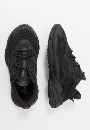 Paire de baskets de sport noires avec détails en mesh et en daim, fermeture à lacets à l'avant, semelles épaisses et rembourrées, vues de dessus et de côté.