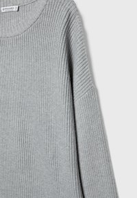 Pull tricoté gris clair à manches longues et col rond, montrant la texture et le motif côtelé.