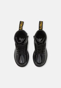 Stivali alla caviglia in pelle verniciata nera con punta tonda, lacci davanti e pratici tiranti gialli con il marchio. Superficie liscia con una finitura lucida a contrasto.