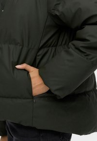 Chaqueta acolchada de color verde oscuro con un diseño acolchado, que cuenta con un bolsillo lateral, textura suave y puños elásticos para un ajuste ceñido.