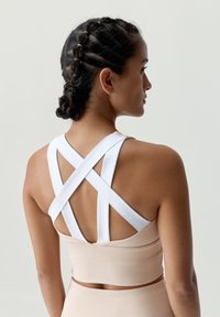 Svetloružový športový podprsenka s bielym krížovým dizajnom na chrbte. Materiál vyzerá hladko s tesným strihom a minimálnymi švami.