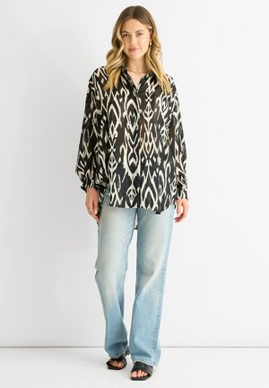 Camicia a maniche lunghe a stampa bianca e nera, taglio loose, abbinata a jeans azzurri chiari e sandali neri. Il tessuto sembra leggero.