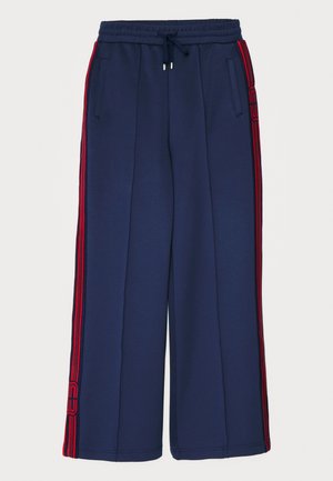 Pantalones de chándal navy con rayas rojas en los laterales, hechos de una tela suave. Tienen una cintura elástica con cordón y bolsillos laterales. Diseño de pierna ancha.