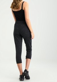 Černý tílko a tmavě šedé capri kalhoty z měkké tkaniny, které mají volný střih a ohrnuté lemy, doplněné černými sportovními botami.
