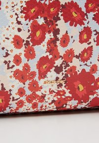 Gros plan sur un tissu à motifs floraux rouges, oranges, blancs et bruns avec un petit texte doré "ESPADRILLE" sur un fond clair.