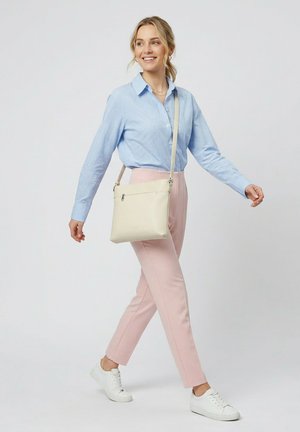 Frau läuft, trägt ein hellblau kariertes Hemd, hellrosa Hose, weiße Turnschuhe und eine beige Umhängetasche.