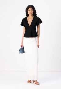 Čierny peplum top s krátkymi volánovými rukávmi, s výstrihom do V, spárovaný s textúrovanou bielou maxi sukňou a otvorenými ružovými sandálmi. Doplnok: malá modrá taška.