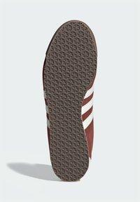 Κόκκινη σόλα αθλητικού παπουτσιού από σουέντ με λευκές ρίγες, που διαθέτει υφή καφέ καουτσούκ εξωτερικής σόλας με γεωμετρικό σχέδιο για καλύτερη πρόσφυση.